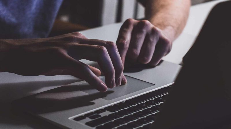 Ein Mann tippt mit seinen Händen auf einer Laptop-Tastatur
